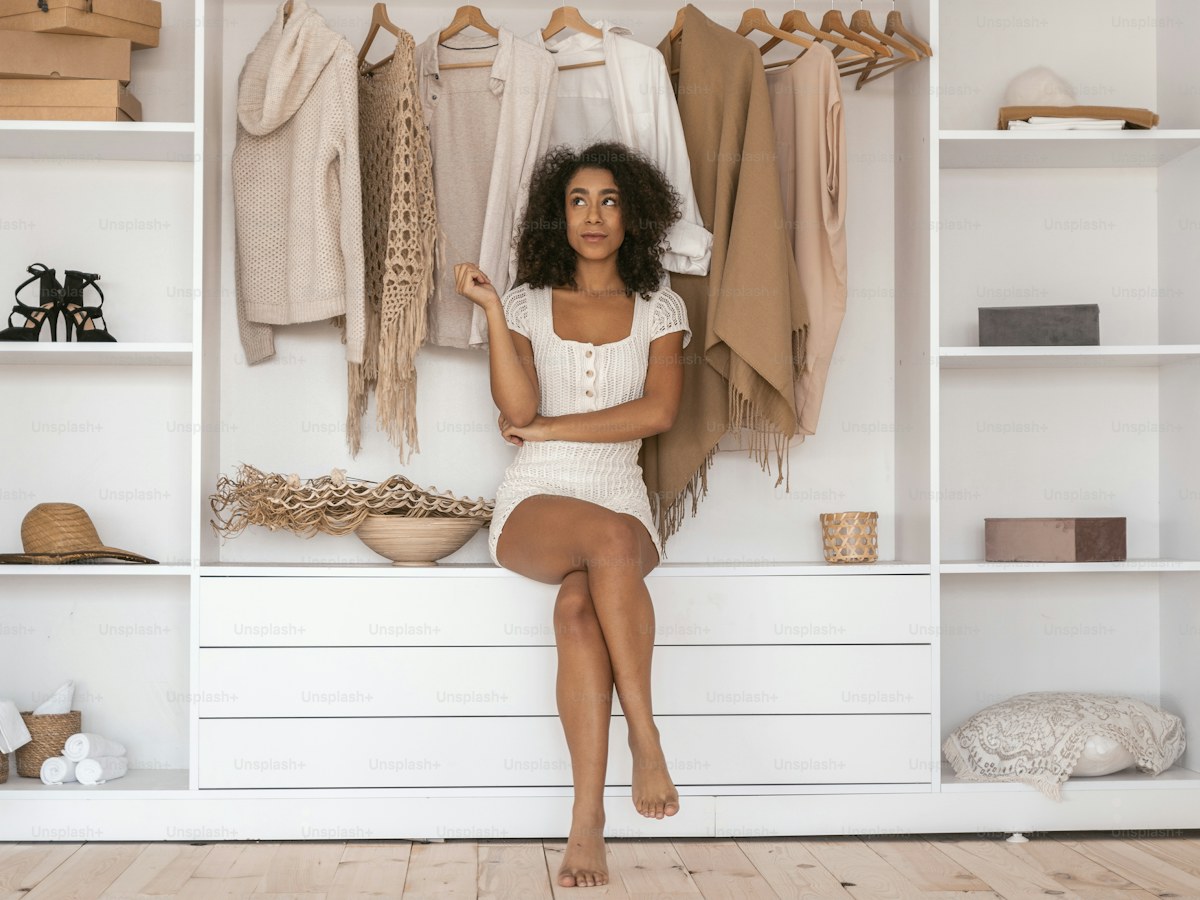 Playful mood. Pleased young female crossing legs while sitting in her wardrobe