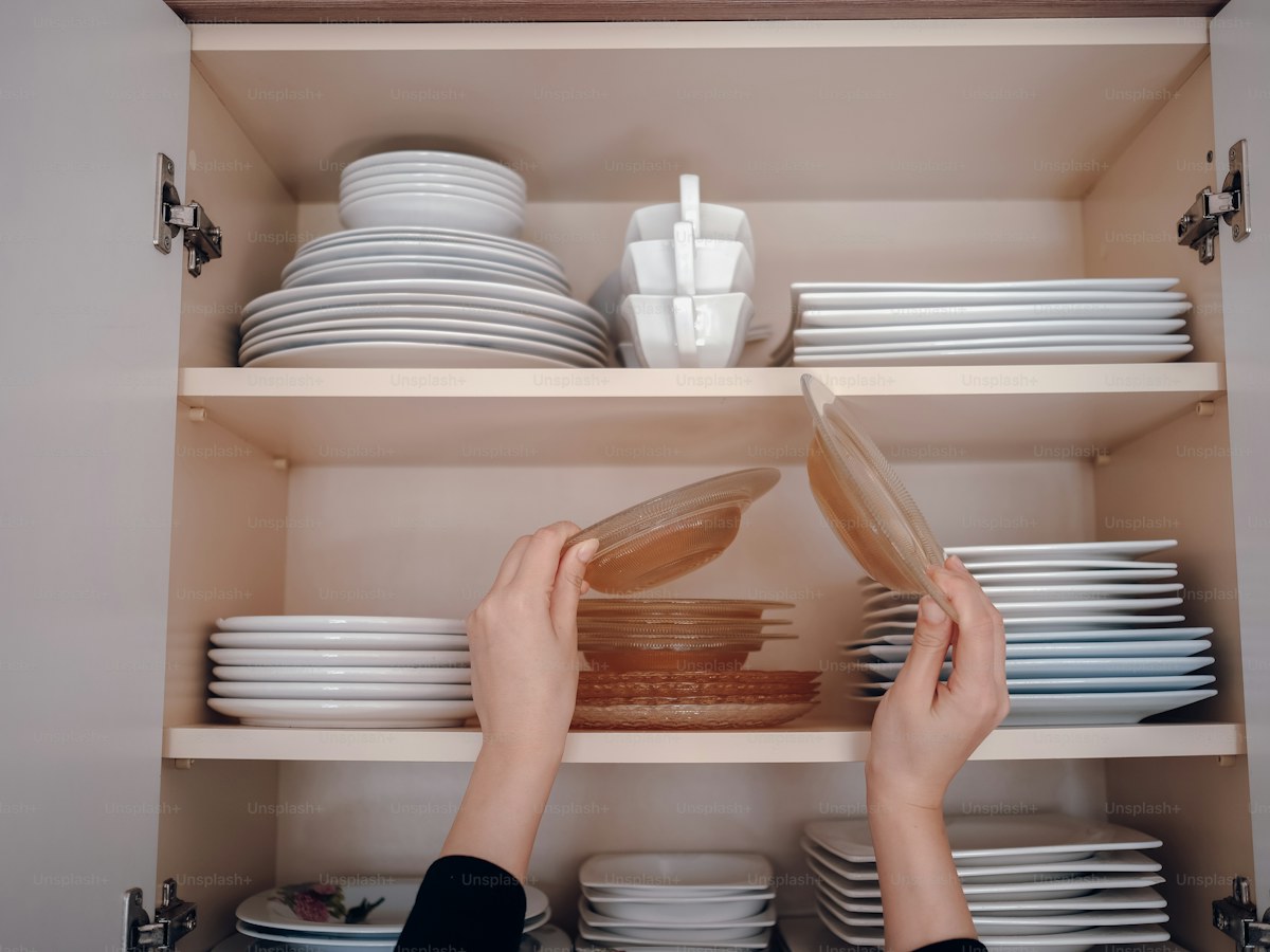 a person is reaching for a plate in a cabinet
