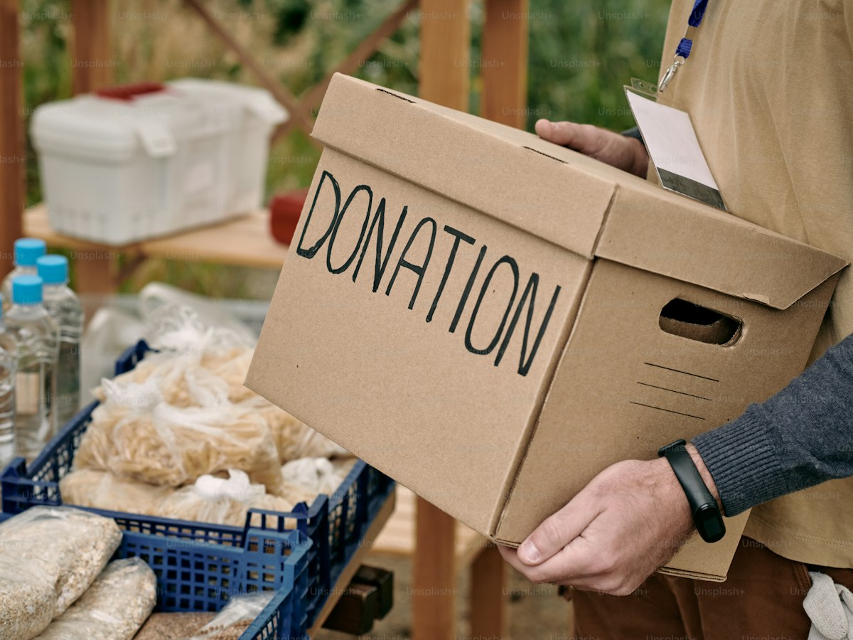 Male volunteer holding packed donation box while standing by table with free food